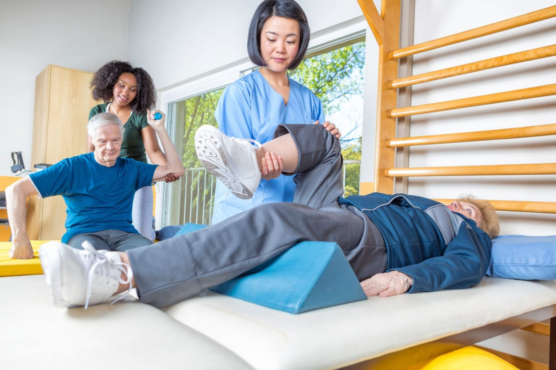 Rehab clinic gym. Multi racial nurses helping elder patients.