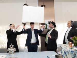 A ceremonial lifting of a Torah scroll by two individuals with others participating, signifying a significant moment in a Jewish religious ceremony.