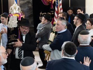 An intimate moment during a Jewish ceremony with individuals carrying a decorated Torah scroll, signifying a procession or celebration within the community.