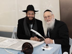 An image capturing a moment between two men at a table with a Torah scroll, indicative of a personal and meaningful ceremony or celebration.