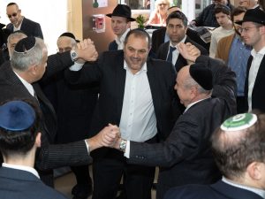 Two men engaging in a traditional Jewish handshake in a crowd, suggesting a moment of congratulations or agreement during a communal event.
