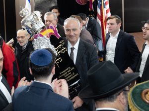 A jubilant moment as a man carries a beautifully adorned Torah scroll through a crowd during a Jewish celebration or procession.