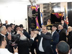 Participants in a Torah scroll ceremony hoisting the ornate scroll, surrounded by an attentive crowd, marking a significant moment in the event.
